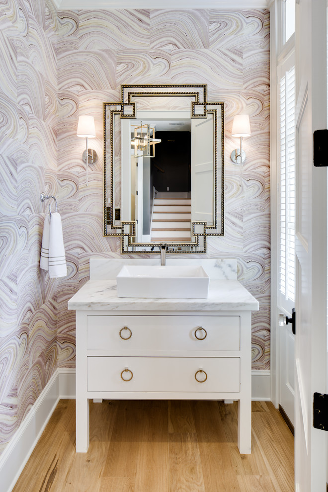 Photo of a traditional powder room in New Orleans with furniture-like cabinets, white cabinets, multi-coloured walls, light hardwood floors, a vessel sink, beige floor and white benchtops.