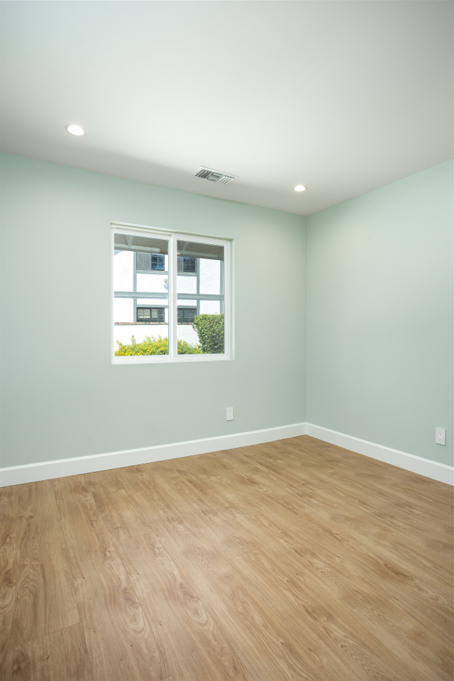 Small transitional guest bedroom in Los Angeles with green walls, laminate floors and brown floor.