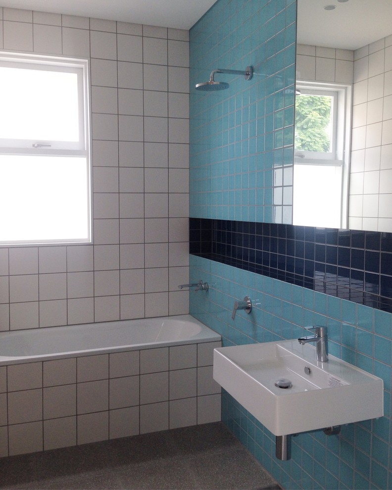 This is an example of a small modern kids bathroom in Sydney with flat-panel cabinets, an alcove tub, an open shower, a wall-mount toilet, blue tile, ceramic tile, blue walls, concrete floors, a wall-mount sink and tile benchtops.