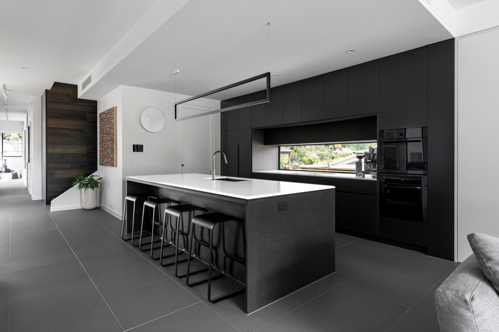 Inspiration for a contemporary galley kitchen in Brisbane with an undermount sink, flat-panel cabinets, black cabinets, black appliances, with island, grey floor and white benchtop.