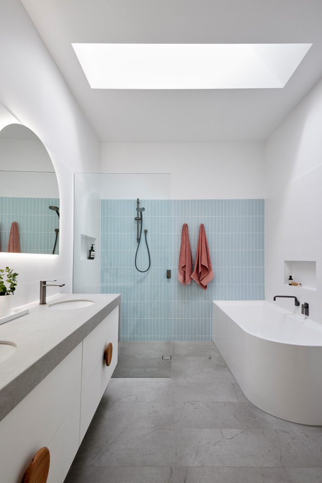 Contemporary bathroom in Melbourne with flat-panel cabinets, white cabinets, a corner bath, a built-in shower, blue tiles, white walls, a submerged sink, grey floors, an open shower, grey worktops, double sinks and a floating vanity unit.