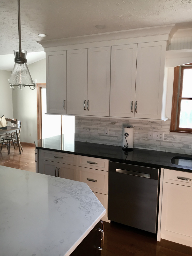 Inspiration for a large transitional single-wall medium tone wood floor eat-in kitchen remodel with an undermount sink, shaker cabinets, white cabinets, granite countertops, multicolored backsplash, marble backsplash, stainless steel appliances, an island and black countertops
