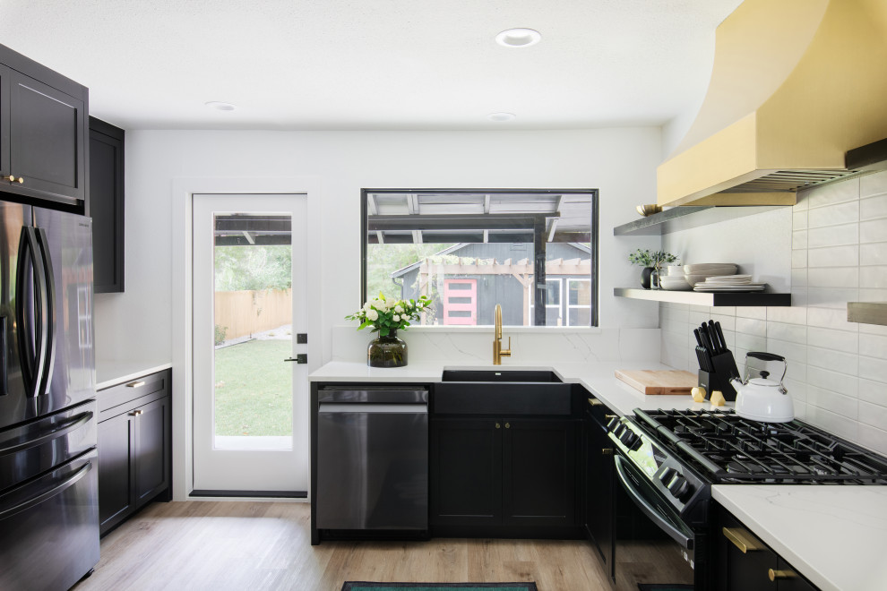 Open concept kitchen - mid-sized transitional u-shaped medium tone wood floor and brown floor open concept kitchen idea in Austin with a farmhouse sink, shaker cabinets, black cabinets, quartz countertops, white backsplash, porcelain backsplash, stainless steel appliances, a peninsula and white countertops