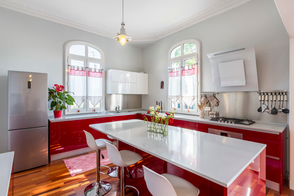 Large contemporary l-shaped eat-in kitchen in Bordeaux with flat-panel cabinets, red cabinets, metallic splashback, metal splashback, stainless steel appliances, medium hardwood floors and with island.