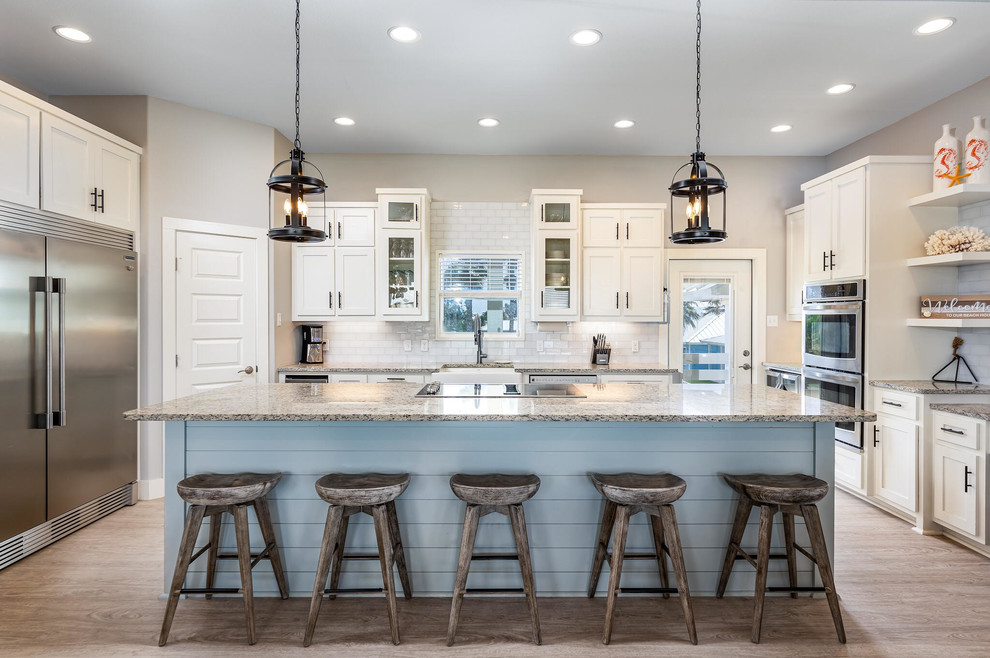 Beach style u-shaped kitchen in Austin with shaker cabinets, white cabinets, white splashback, stainless steel appliances, with island and grey benchtop.