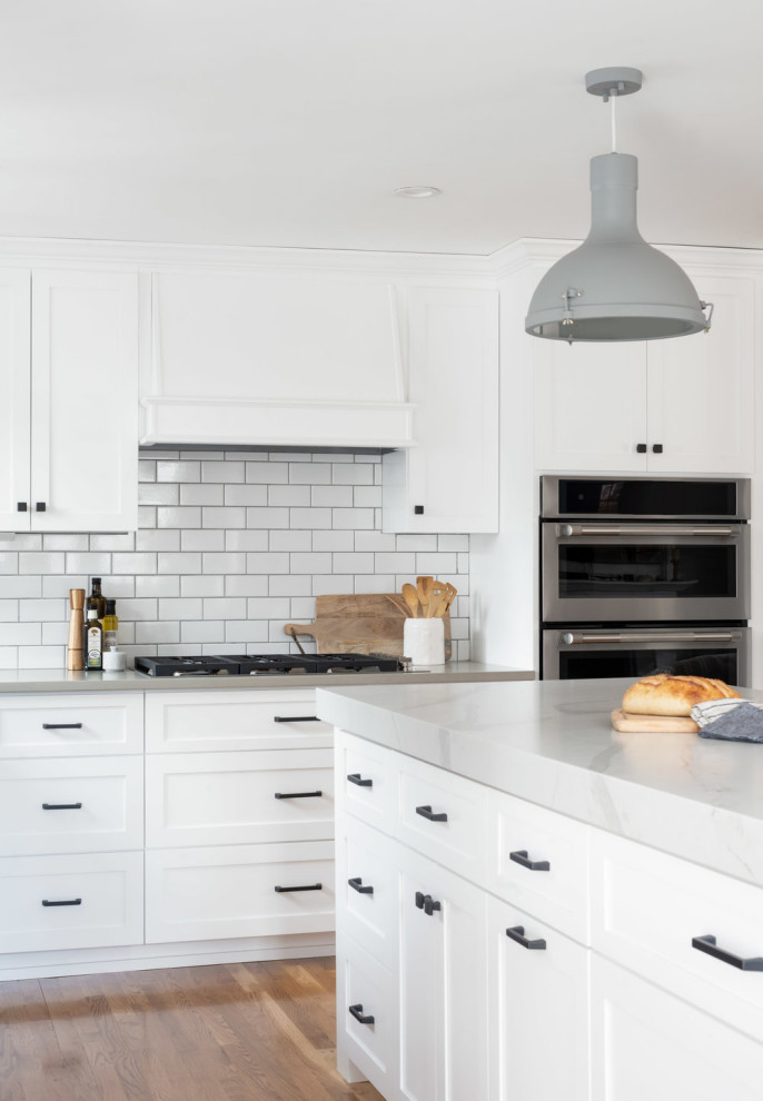 Mid-sized transitional u-shaped eat-in kitchen in Boston with an undermount sink, shaker cabinets, white cabinets, quartz benchtops, white splashback, subway tile splashback, stainless steel appliances, light hardwood floors, with island, beige floor and grey benchtop.