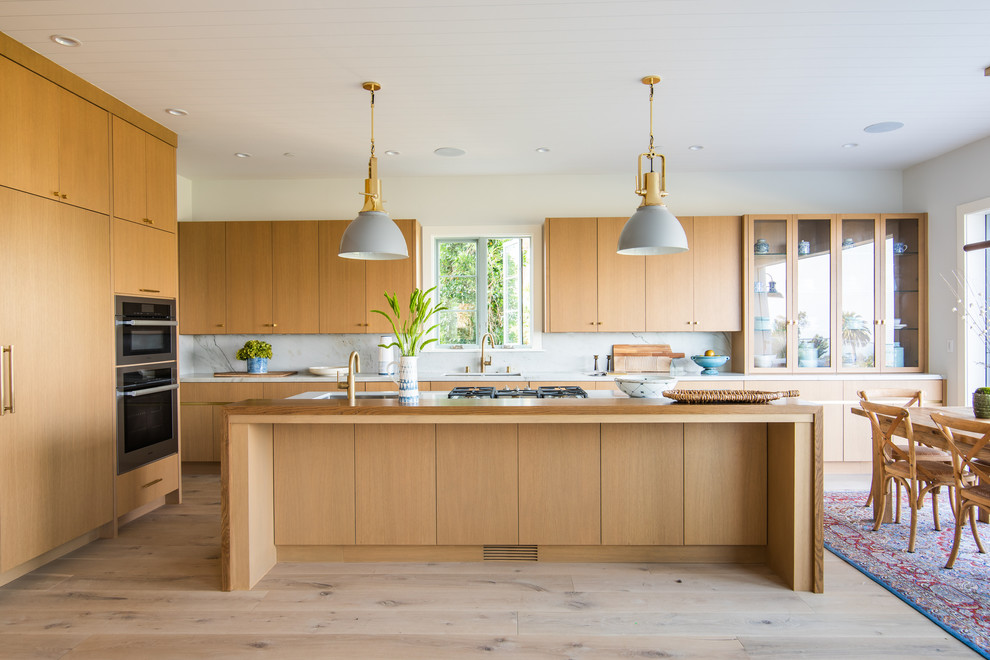 Large beach style l-shaped eat-in kitchen in Los Angeles with flat-panel cabinets, medium wood cabinets, marble benchtops, grey splashback, marble splashback, stainless steel appliances, light hardwood floors, with island, grey benchtop, an undermount sink and beige floor.