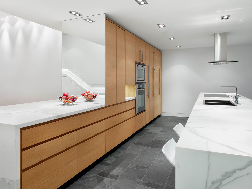 This is an example of a mid-sized contemporary galley open plan kitchen in Toronto with flat-panel cabinets, medium wood cabinets, stainless steel appliances, with island, an undermount sink, marble benchtops, slate floors and grey floor.