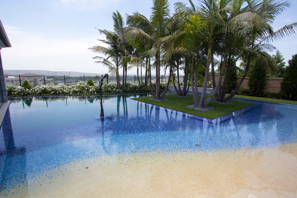 This is an example of a large beach style backyard custom-shaped pool in Orange County with a water feature and tile.