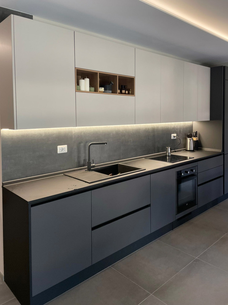 This is an example of a medium sized contemporary single-wall kitchen/diner in Other with an integrated sink, flat-panel cabinets, grey cabinets, laminate countertops, grey splashback, porcelain splashback, black appliances, porcelain flooring, no island, grey floors and black worktops.