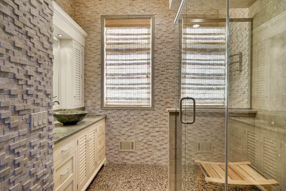 Mid-sized contemporary 3/4 bathroom in New York with beige cabinets, pebble tile floors, a vessel sink, louvered cabinets, a corner shower, gray tile, stone tile, grey walls, multi-coloured floor and a hinged shower door.