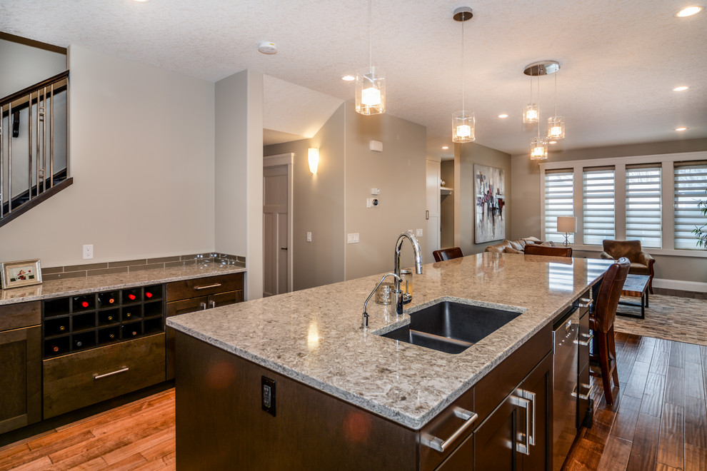Large transitional l-shaped medium tone wood floor open concept kitchen photo in Calgary with an undermount sink, shaker cabinets, white cabinets, granite countertops, gray backsplash, porcelain backsplash, stainless steel appliances and an island