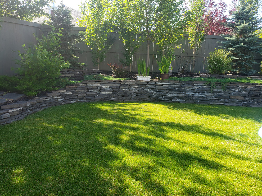 Photo of a mid-sized rustic partial sun backyard stone retaining wall landscape in Edmonton for summer.