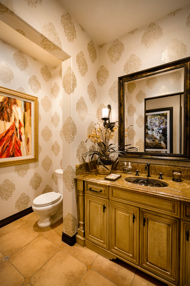Design ideas for a mid-sized mediterranean powder room in Other with raised-panel cabinets, medium wood cabinets, a two-piece toilet, beige walls, porcelain floors, an undermount sink, granite benchtops, brown floor and brown benchtops.