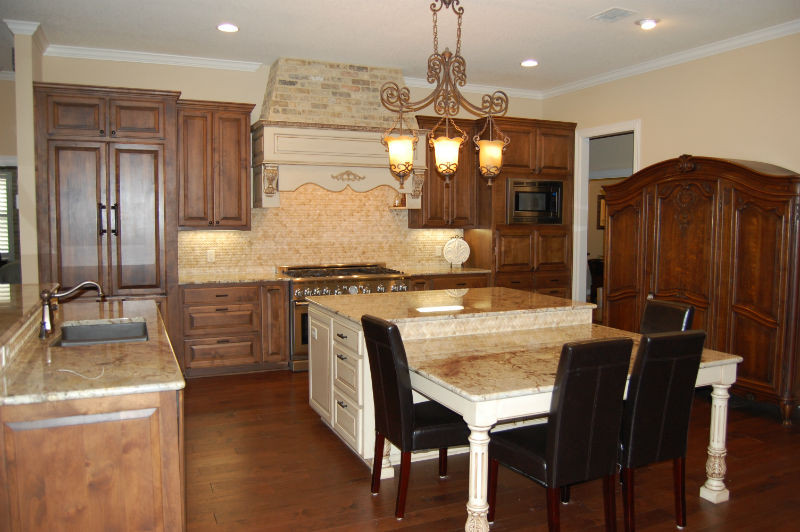 This is an example of a large open plan kitchen in Austin with an undermount sink, raised-panel cabinets, brown cabinets, granite benchtops, travertine splashback, ceramic floors and multiple islands.