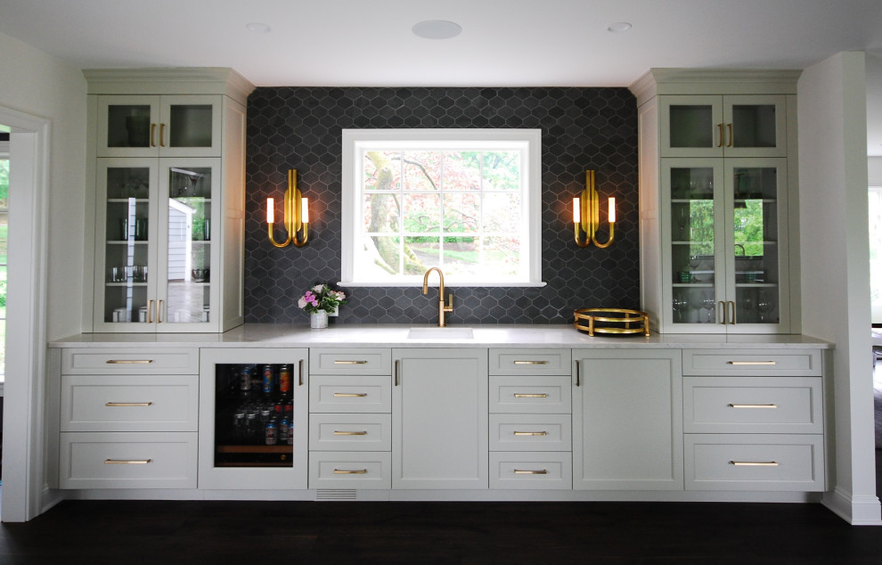 Large transitional single-wall dark wood floor and brown floor wet bar photo with an undermount sink, shaker cabinets, beige cabinets, quartzite countertops, black backsplash, porcelain backsplash and beige countertops
