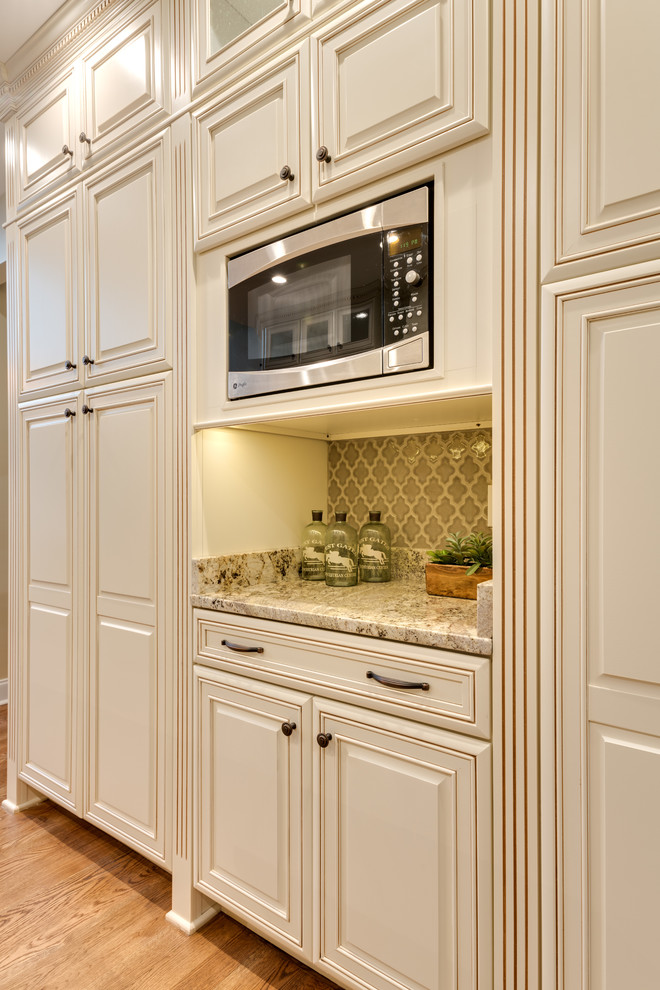 Photo of a mid-sized traditional u-shaped eat-in kitchen in Atlanta with an undermount sink, raised-panel cabinets, granite benchtops, beige splashback, stainless steel appliances, light hardwood floors, with island, beige cabinets, porcelain splashback, brown floor and beige benchtop.