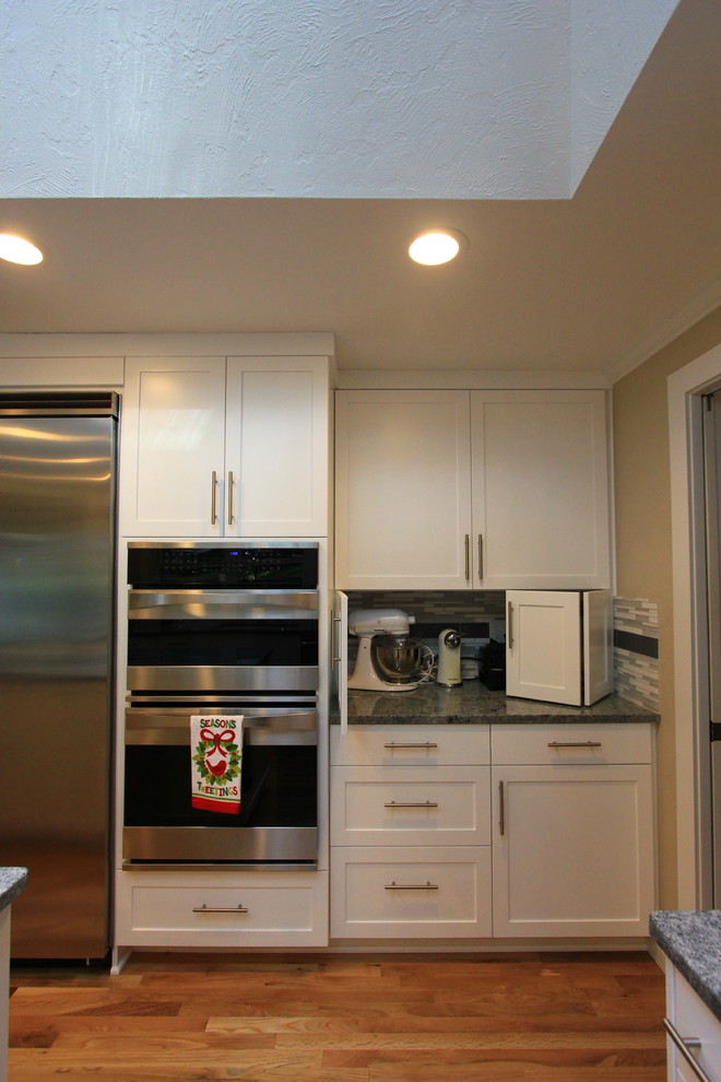 Open concept kitchen - large transitional u-shaped light wood floor open concept kitchen idea with an undermount sink, shaker cabinets, white cabinets, granite countertops, multicolored backsplash, mosaic tile backsplash, stainless steel appliances and an island