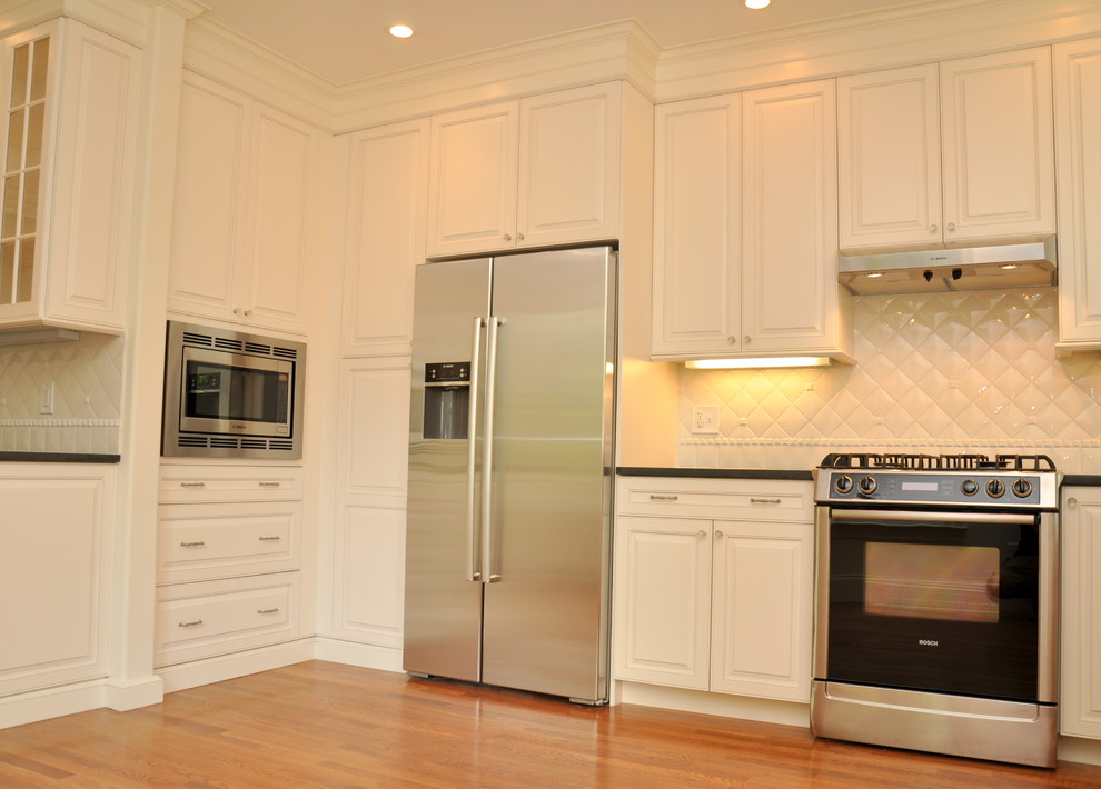 Photo of a mid-sized traditional l-shaped separate kitchen in Boston with an undermount sink, raised-panel cabinets, white cabinets, granite benchtops, white splashback, porcelain splashback, stainless steel appliances, medium hardwood floors and no island.