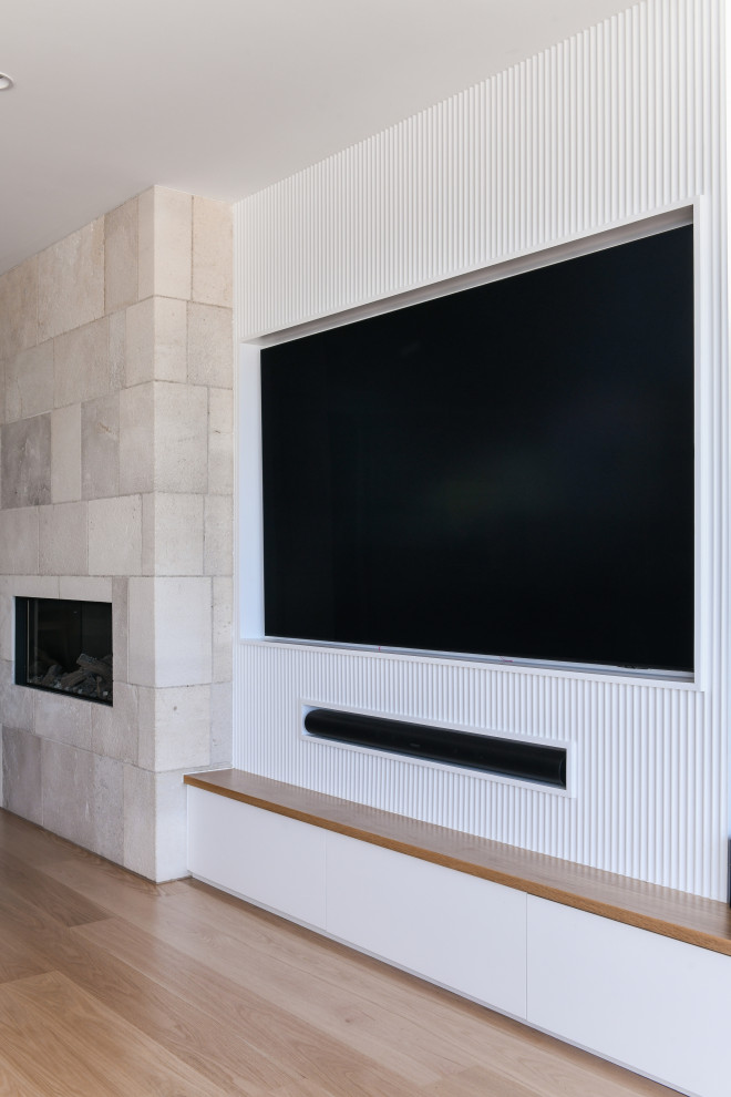 This is an example of a large coastal open plan living room in Sydney with white walls, medium hardwood flooring, a standard fireplace, a stone fireplace surround and a built-in media unit.