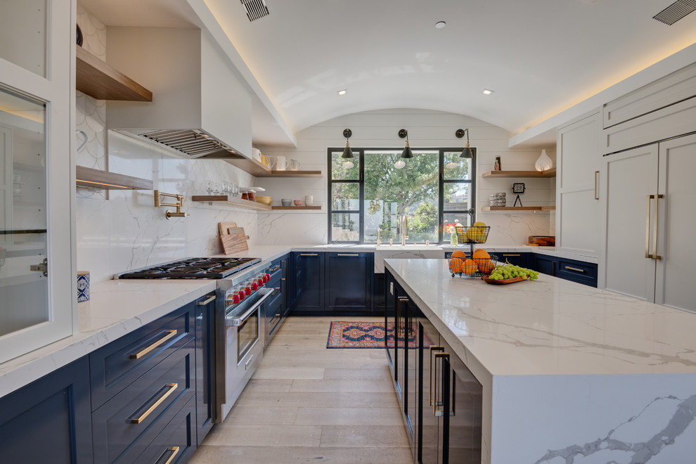 Photo of a transitional u-shaped kitchen in Los Angeles with shaker cabinets, blue cabinets, white splashback, panelled appliances, light hardwood floors, with island, beige floor and white benchtop.