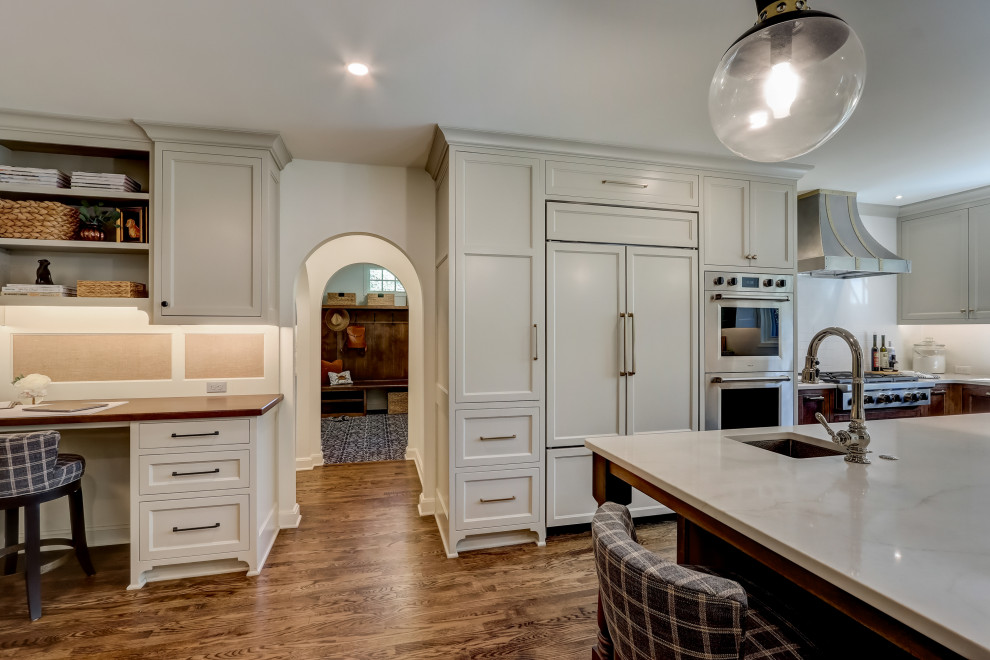 Inspiration for a mid-sized transitional l-shaped medium tone wood floor and brown floor enclosed kitchen remodel in Milwaukee with an undermount sink, recessed-panel cabinets, medium tone wood cabinets, quartz countertops, white backsplash, ceramic backsplash, stainless steel appliances, an island and white countertops