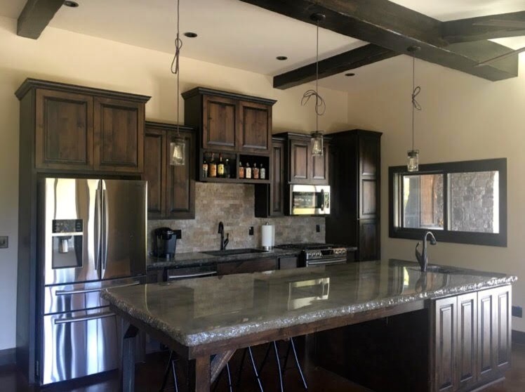 Large transitional u-shaped brown floor enclosed kitchen photo in Orange County with an undermount sink, raised-panel cabinets, dark wood cabinets, concrete countertops, beige backsplash, stone tile backsplash, stainless steel appliances and an island