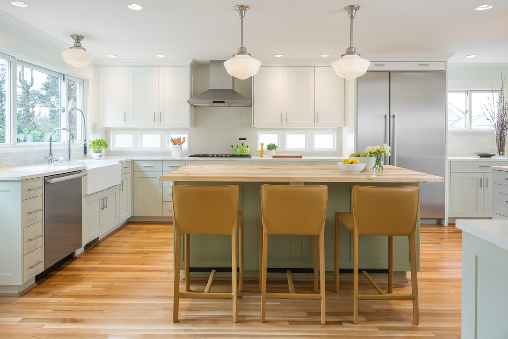 Example of a transitional l-shaped medium tone wood floor and brown floor eat-in kitchen design in Seattle with a farmhouse sink, recessed-panel cabinets, subway tile backsplash, stainless steel appliances, an island, quartzite countertops, green cabinets, white backsplash and white countertops
