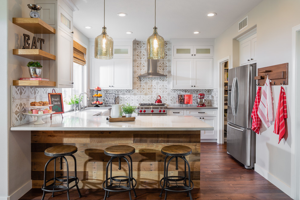 Mid-sized country u-shaped kitchen in Los Angeles with a farmhouse sink, shaker cabinets, white cabinets, multi-coloured splashback, stainless steel appliances, medium hardwood floors, a peninsula, white benchtop, quartz benchtops and brown floor.