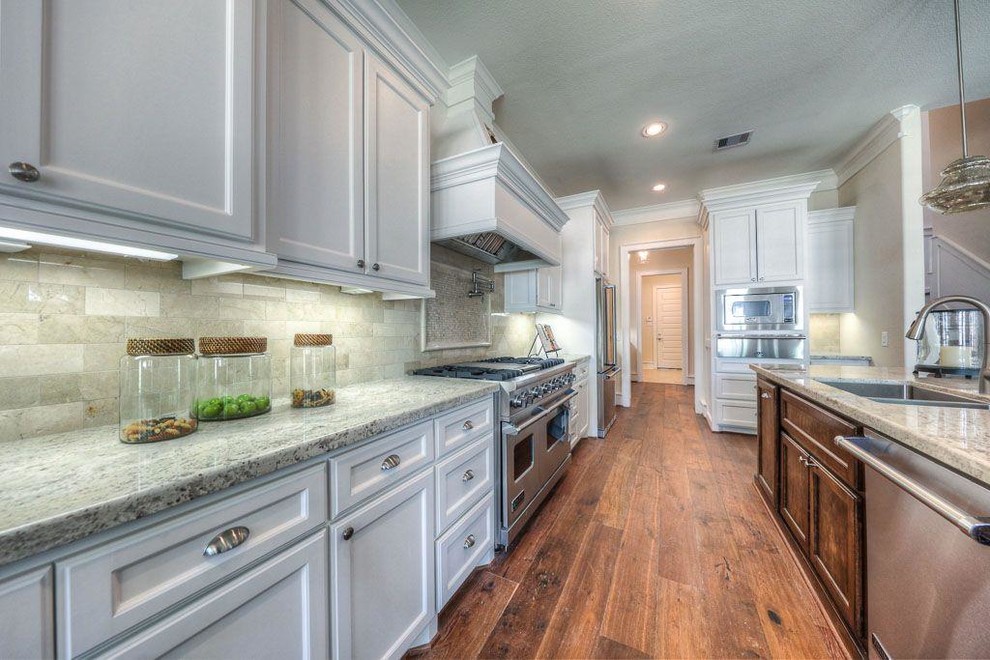 Eat-in kitchen - mid-sized transitional medium tone wood floor eat-in kitchen idea in Houston with a drop-in sink, shaker cabinets, white cabinets, granite countertops, beige backsplash, stone tile backsplash, stainless steel appliances and an island