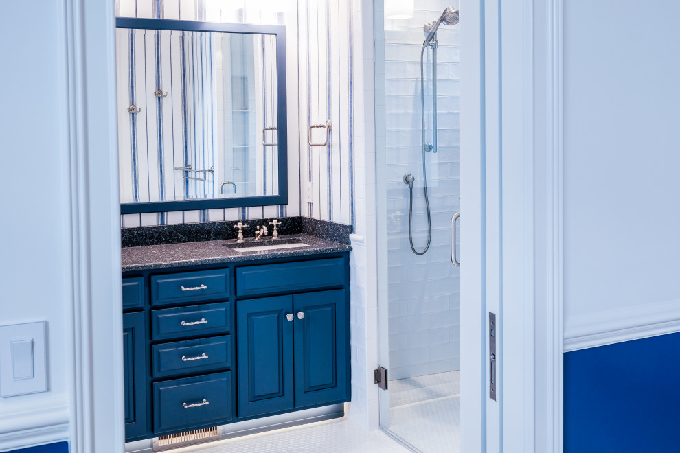 Inspiration for a mid-sized traditional bathroom in Other with raised-panel cabinets, a freestanding tub, a one-piece toilet, ceramic tile, blue walls, ceramic floors, an undermount sink, solid surface benchtops, white floor, blue cabinets, an alcove shower, white tile, a hinged shower door and grey benchtops.
