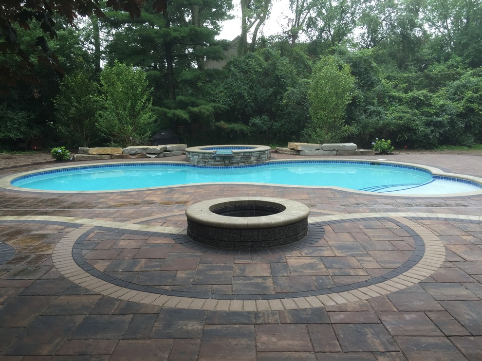 Design ideas for a transitional backyard custom-shaped pool in Detroit with a hot tub and brick pavers.
