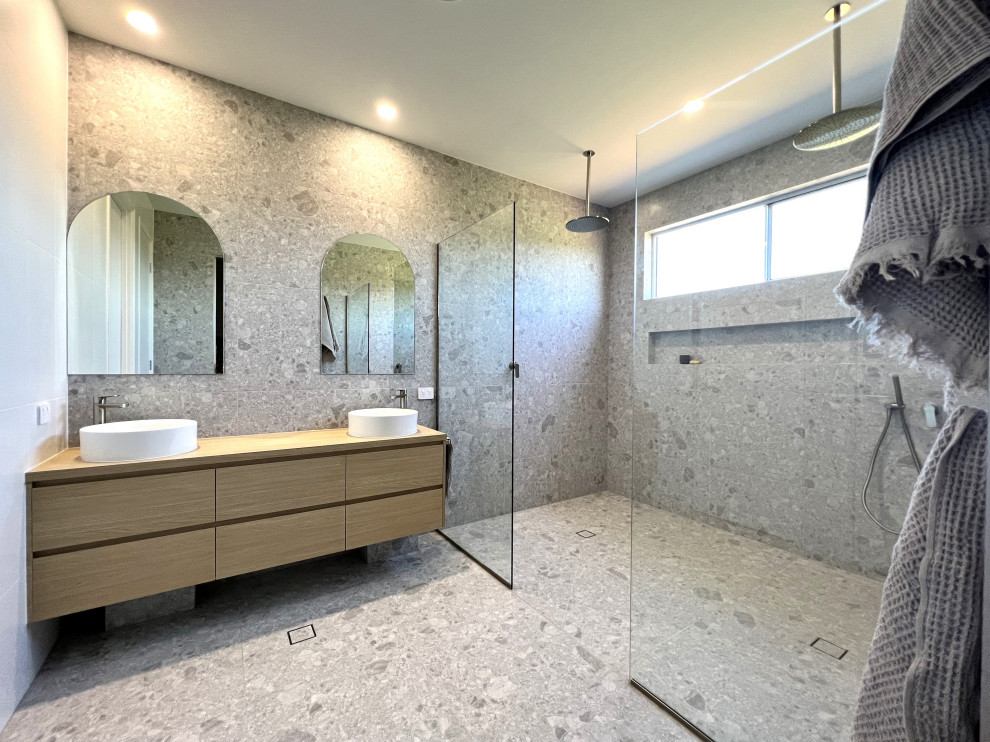Foto på ett funkis en-suite badrum, med släta luckor, skåp i ljust trä, en dubbeldusch, grå kakel, klinkergolv i keramik, ett fristående handfat, laminatbänkskiva, grått golv och med dusch som är öppen
