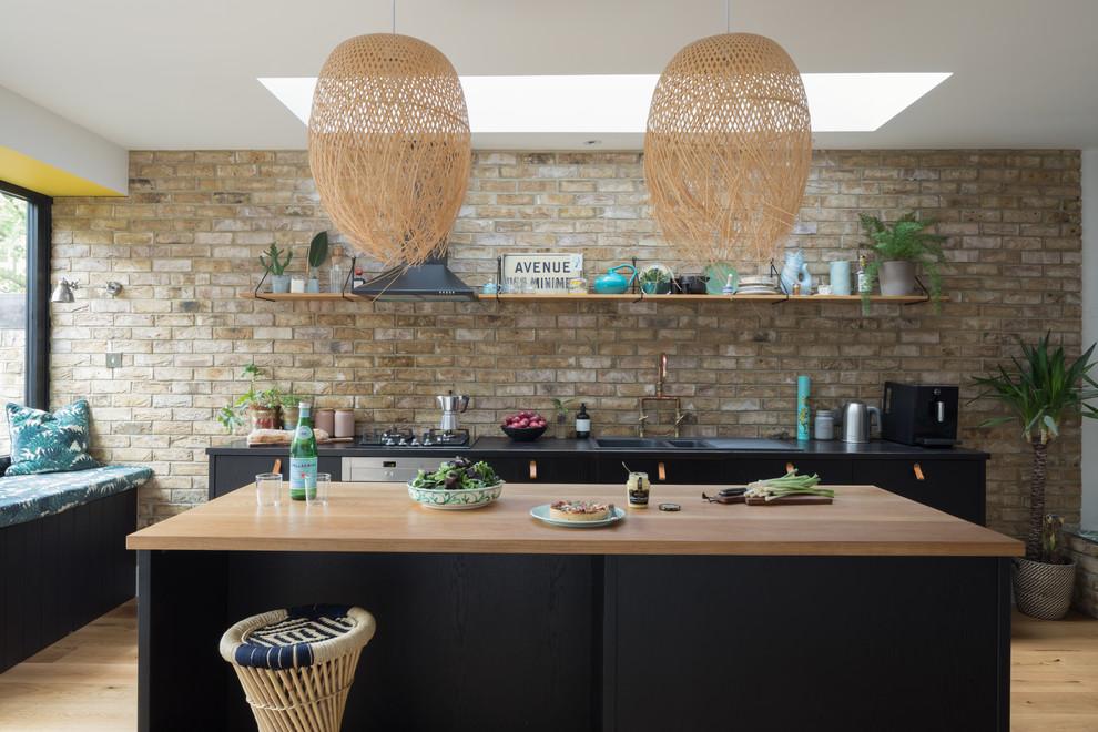 Beach style single-wall kitchen with a double-bowl sink, flat-panel cabinets, black cabinets, wood benchtops, brown splashback, brick splashback, light hardwood floors, with island, beige floor and beige benchtop.