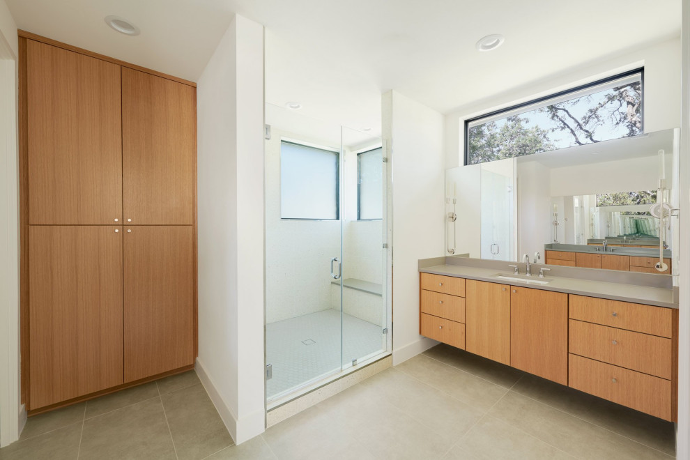 Photo of a mid-sized midcentury master bathroom in Austin with flat-panel cabinets, medium wood cabinets, a corner shower, a one-piece toilet, white tile, porcelain tile, white walls, porcelain floors, an undermount sink, engineered quartz benchtops, grey floor, a hinged shower door, grey benchtops, a shower seat, a double vanity and a floating vanity.