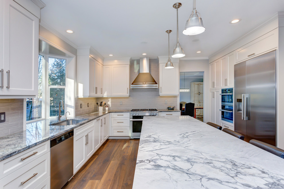Large transitional u-shaped medium tone wood floor and brown floor enclosed kitchen photo in Vancouver with an undermount sink, shaker cabinets, white cabinets, granite countertops, gray backsplash, porcelain backsplash, stainless steel appliances, an island and gray countertops
