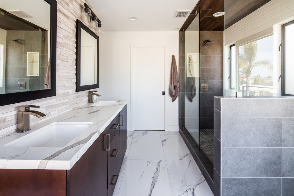 This is an example of a large contemporary master bathroom in San Diego with flat-panel cabinets, brown cabinets, a double shower, gray tile, stone tile, white walls, porcelain floors, a drop-in sink, quartzite benchtops, white floor, a sliding shower screen, white benchtops, an enclosed toilet, a double vanity and a built-in vanity.