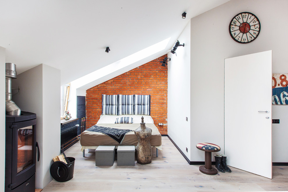 This is an example of an industrial master bedroom in Moscow with white walls, light hardwood floors and a wood stove.