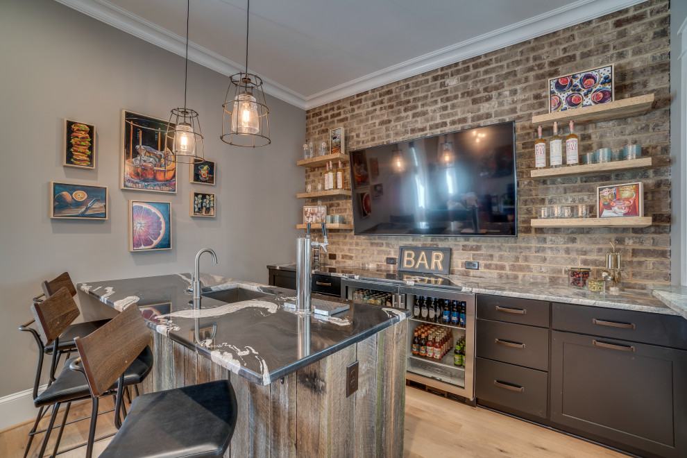 Country galley seated home bar in Richmond with a drop-in sink, shaker cabinets, black cabinets, marble benchtops, brick splashback, light hardwood floors and black benchtop.