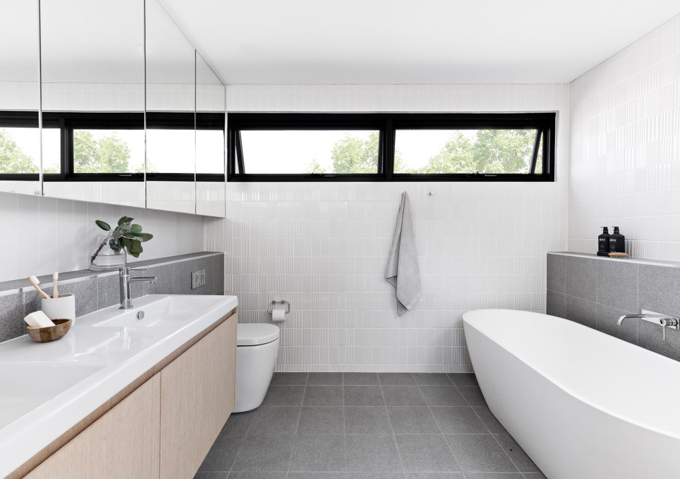 Design ideas for a mid-sized contemporary master bathroom in Sydney with light wood cabinets, a freestanding tub, white tile, gray tile, ceramic tile, white walls, porcelain floors, grey floor, a double vanity, a floating vanity, flat-panel cabinets, a console sink and white benchtops.