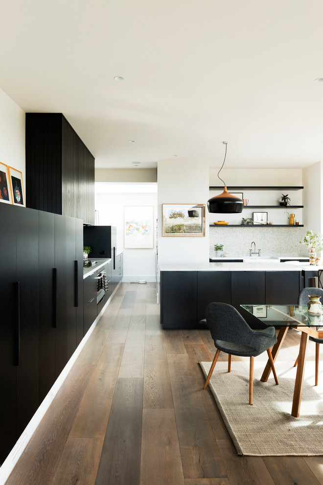 This is an example of a contemporary galley open plan kitchen in Melbourne with a farmhouse sink, flat-panel cabinets, black cabinets, white splashback, medium hardwood floors and a peninsula.
