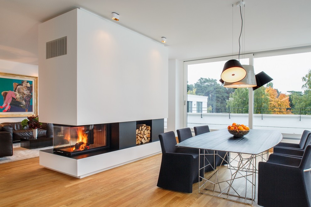 Photo of a large contemporary open plan dining in Berlin with white walls, light hardwood floors, a two-sided fireplace, a plaster fireplace surround and beige floor.