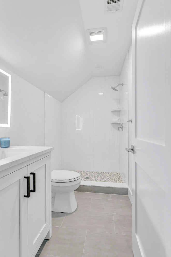 Bild på ett litet lantligt vit vitt badrum med dusch, med vita skåp, en hörndusch, en toalettstol med separat cisternkåpa, vit kakel, vita väggar, klinkergolv i porslin, ett undermonterad handfat, grått golv och dusch med duschdraperi