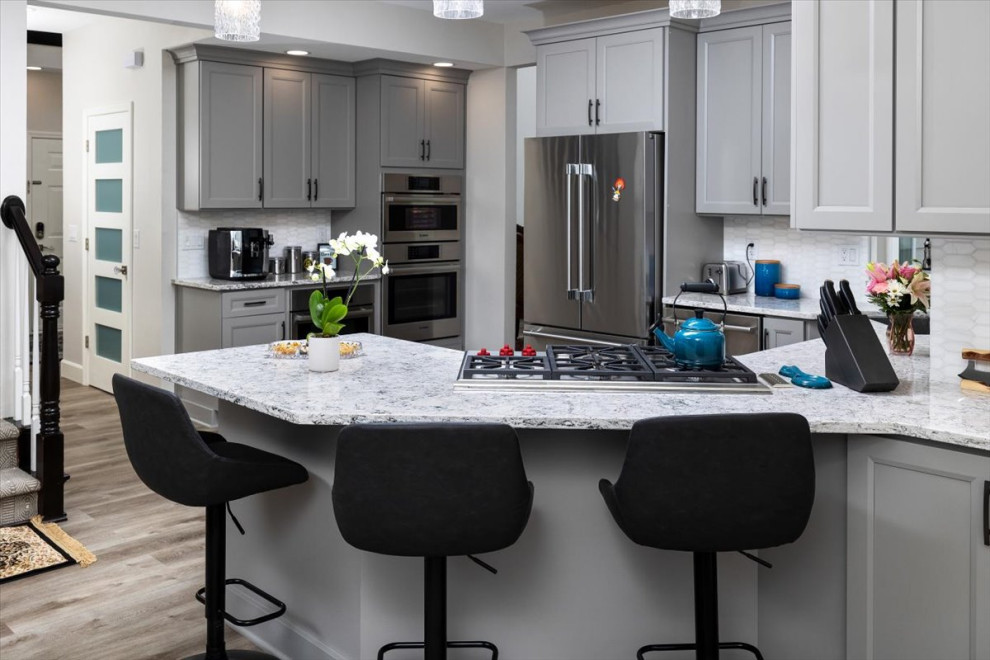 Open concept kitchen - mid-sized transitional laminate floor and gray floor open concept kitchen idea with recessed-panel cabinets, gray cabinets, quartz countertops, white backsplash, marble backsplash, stainless steel appliances and white countertops