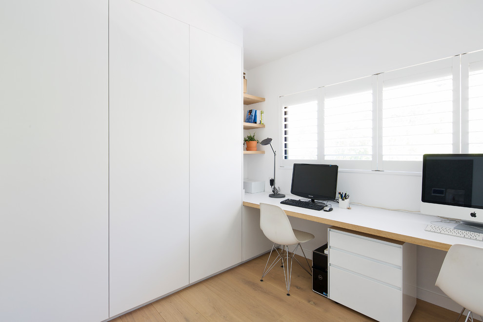 Contemporary home office in Sydney with white walls, medium hardwood floors, a built-in desk and brown floor.