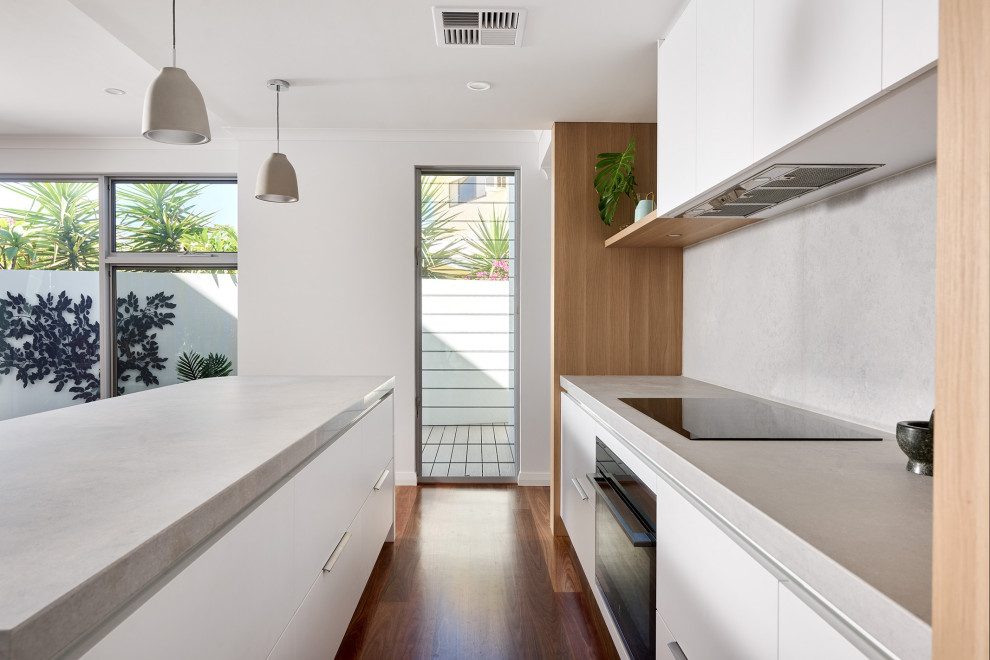 This is an example of a large scandinavian l-shaped eat-in kitchen in Perth with a double-bowl sink, flat-panel cabinets, white cabinets, quartz benchtops, grey splashback, engineered quartz splashback, black appliances, medium hardwood floors, with island, brown floor and grey benchtop.