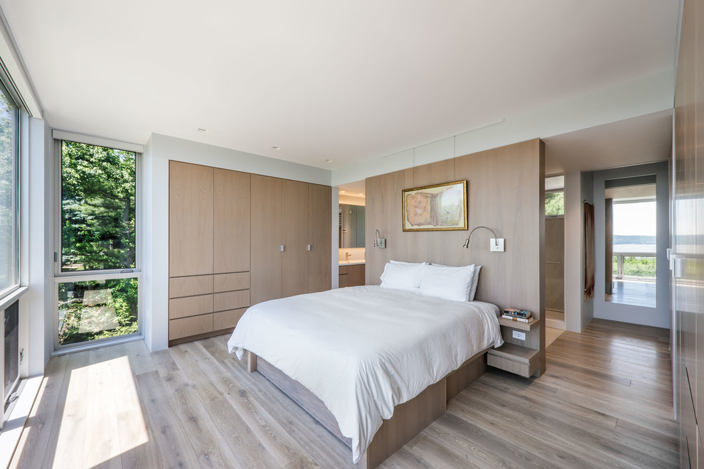 This is an example of a contemporary master bedroom in New York with light hardwood floors and no fireplace.