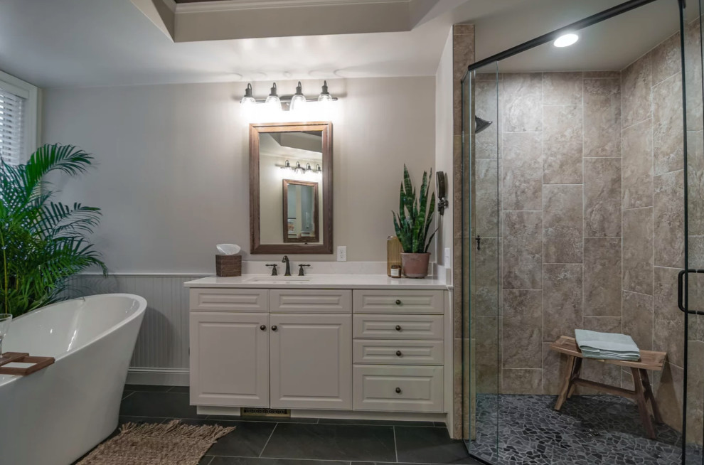 This is an example of a large transitional master bathroom in Minneapolis with shaker cabinets, white cabinets, a freestanding tub, a curbless shower, a one-piece toilet, beige tile, ceramic tile, beige walls, ceramic floors, an undermount sink, engineered quartz benchtops, black floor, a hinged shower door, white benchtops, a niche, a double vanity, a built-in vanity, timber and decorative wall panelling.