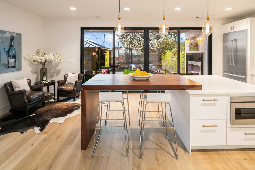 Example of a trendy light wood floor and beige floor eat-in kitchen design in Seattle with an undermount sink, flat-panel cabinets, white cabinets, white backsplash, stainless steel appliances, an island and white countertops