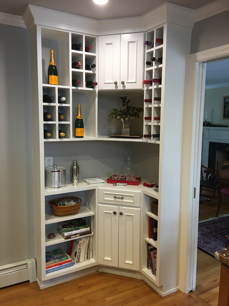 Photo of a mid-sized traditional l-shaped wet bar in New York with no sink, beaded inset cabinets, white cabinets, wood benchtops, medium hardwood floors and brown floor.